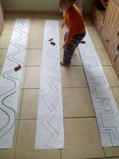 a little boy standing on the floor in front of some cut out paper with lines