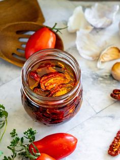 a jar filled with pickled tomatoes next to garlic and other vegetables on a counter