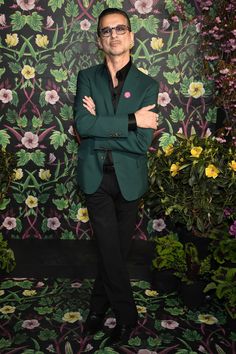 a man in a green suit and black shirt standing with his arms crossed against his chest