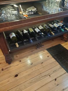 a wooden table topped with lots of bottles of wine next to a shelf filled with glasses