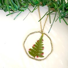 a fern leaf is in a circle on a gold plated necklace with red flowers