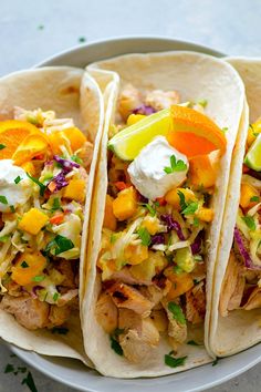 three tacos with chicken, coleslaw and sour cream on them sitting on a plate