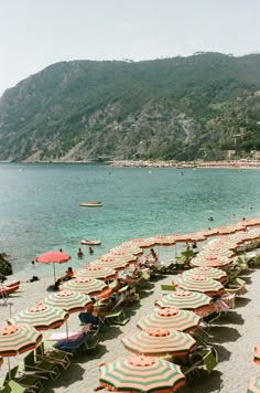 many umbrellas and chairs are lined up on the beach with mountains in the background