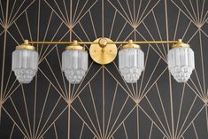 three lights are hanging on the wall in front of an art deco design pattern with gold accents