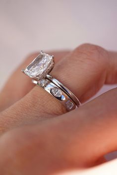 a woman's hand with a diamond ring on top of her finger and an engagement band