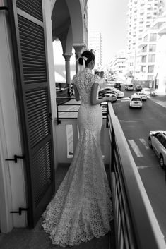 a woman in a long dress standing on a balcony looking out at the city street