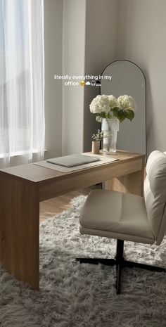 a desk with a mirror, chair and flowers on it in front of a window