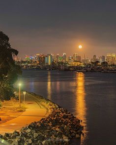 a full moon is seen over the city skyline from across the water at night time