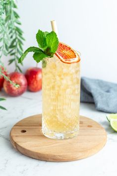 a drink with an orange slice and mint garnish sitting on a cutting board