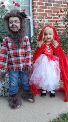 two children dressed up in costumes standing next to each other on the side of a house