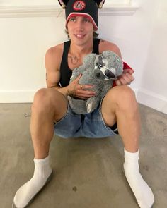 a woman sitting on the floor holding a stuffed animal in her hands and wearing a hat