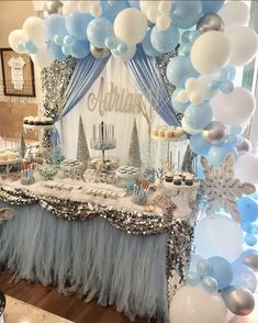 a table topped with lots of balloons and desserts next to a wall covered in snowflakes