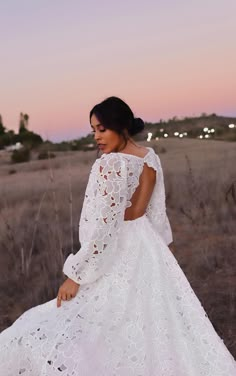 a woman in a white dress is sitting on a rock and looking off into the distance