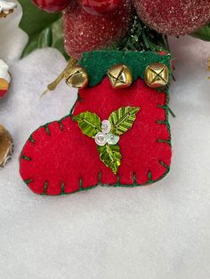 a christmas stocking ornament with bells and holly on it sitting in the snow