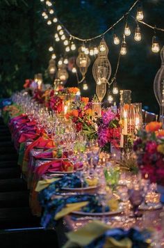 a long table covered in lots of glasses and plates with lit candles on top of them