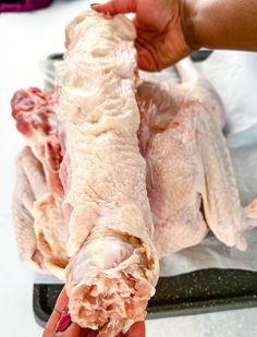 two hands holding up raw chicken in front of a pan with other meats on it