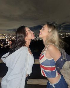 two beautiful young women standing next to each other in front of a cityscape