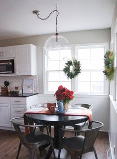 a dining room table with chairs and a vase filled with red flowers on top of it