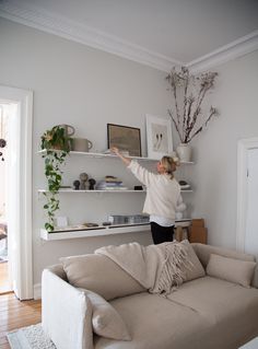 a woman standing in the middle of a living room with her arms up and she is reaching for something