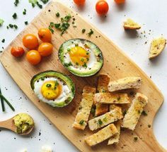 an avocado cut in half on a cutting board next to tomatoes and bread