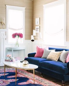 a living room with blue couches and pink pillows on the rug in front of two windows