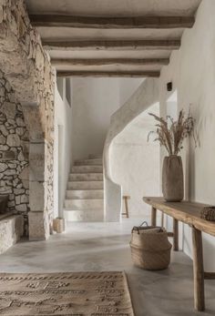 a room with stone walls and flooring next to a wooden table in front of a stair case