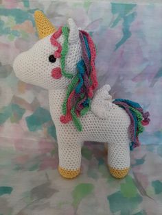 a crocheted stuffed unicorn with multicolored mane and tail sitting on a floral background