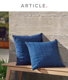 two blue pillows sitting on top of a wooden bench next to a potted plant