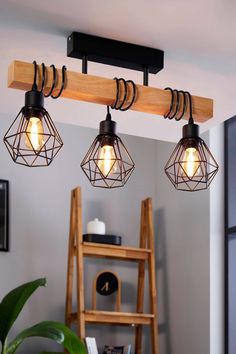 three light fixtures hanging from a wooden beam in a room with a ladder and window