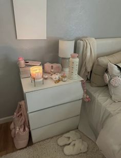 a bedroom with a white bed and pink shoes on the dresser next to it is lit by a candle