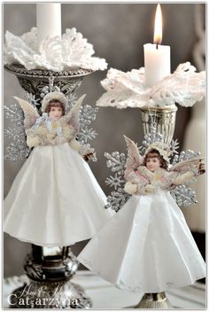 two paper angel ornaments sitting on top of a table next to a candle holder with a lit candle in it