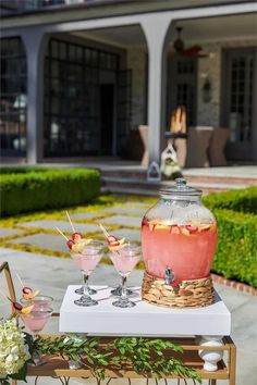 a table topped with drinks next to a garden filled with flowers and greenery in front of a house