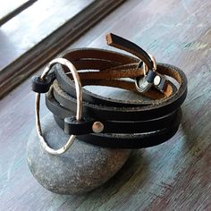 "This wrap statement bracelet is the perfect addition to your jewelry staples. Made with 1/4\" strips of handcut leather and featuring a 1 1/2\" hammered ring in either antique brass or antique silver secured with matching rivets. The bracelet wraps around the wrist 4 times and secures with an adjustable closure. I use only genuine U.S. tanned leather from either Horween (Chicago) or Wickett and Craig (Pennsylvania). The leather will age beautifully, become buttery soft and develop fabulous char Modern Adjustable Double Band Jewelry, Adjustable Hand Wrapped Leather Wrap Bracelet, Modern Adjustable Jewelry With Black Band, Adjustable Modern Leather Bangle Bracelet, Modern Adjustable Leather Bangle Bracelet, Modern Adjustable Double Band Bracelets, Adjustable Leather Jewelry With Black Band, Adjustable Hand Wrapped Leather Bracelet, Modern Adjustable Cuff Bracelet With Leather Strap