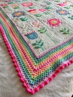 a multicolored crocheted blanket on top of a white bed with pink, green, yellow and blue trim