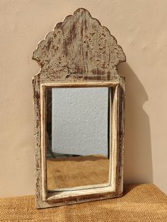 an old wooden mirror sitting on top of a brown cloth covered table next to a wall