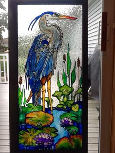 a stained glass window with a blue heron and lily pads on the bottom, in front of a house