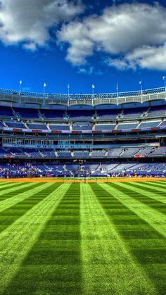 an empty baseball stadium filled with lots of green grass and blue skies in the background