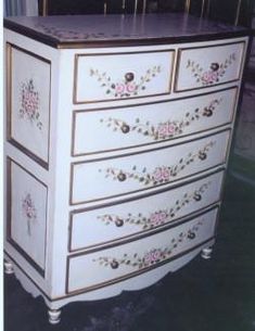 a white dresser with pink flowers painted on it's sides and gold trimmings