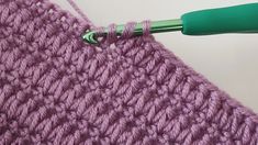 the crochet stitch is being worked on with a green handled knitting needle in front of it