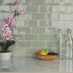 a bowl of fruit sitting on top of a counter next to two bottles and a vase filled with flowers