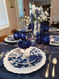 a table set with blue and white plates, silverware and flowers in vases