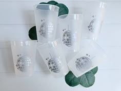 six shot glasses sitting on top of each other next to some green leafy plants