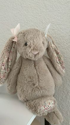 a stuffed rabbit sitting on top of a table next to a wall with white paint