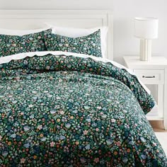 a bed with a green floral comforter and white pillows