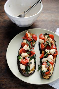 a white plate topped with two stuffed eggplant halves covered in veggies