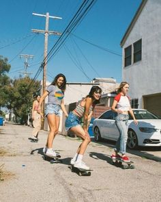 three girls are riding skateboards down the street