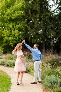 a man and woman dancing on a path in the middle of a park with trees