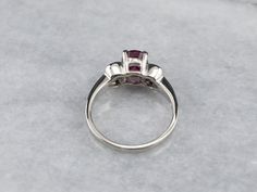 Always in style, rings such as this one can be worn as engagement rings, birthstone rings, or just for special occasions. We've set the center of this one with a high-quality, glowing red ruby. The side stones are bright white diamonds, reflecting plenty of light into the center stone. As an engagement ring will look well with a variety of bands, from a plain golden circle to a ruby and diamond eternity band. Metal: 14K White Gold Gem: Ruby 2.02 Carats Gem Measurements: 8.0 x 6.0 mm, Oval Accents: 8 Diamonds totaling .50 Carats, G in Color, SI1 in Clarity Ring Size: 6.75 Marks: “14K MFP” Stamped on the inside band Formal Red Ruby Ring With Three Stones, Formal Ruby Three Stone Ring, Formal Red Three Stone Ruby Ring, Ruby Ring With Center Stone For Promise, Ruby Diamond Ring With Accent Stones And Round Cut, Anniversary Ruby Ring With Center Stone In Round Band, Promise Ruby Ring With Round Cut Center Stone, Ruby Anniversary Ring With Center Stone, Promise Ruby Ring With Center Stone