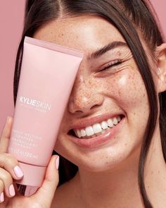 a woman holding up a tube of skin cream to her face