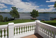 a balcony with white railings overlooks a lake and green grass on the other side